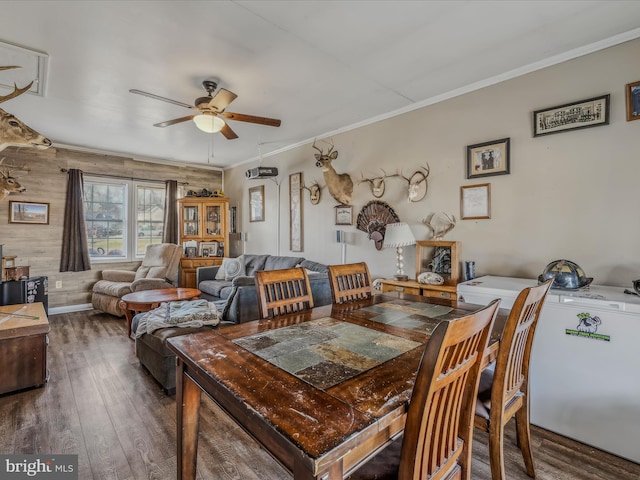 dining room with ceiling fan, wooden walls, dark wood-type flooring, and ornamental molding