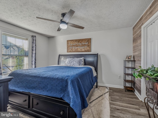 bedroom with ceiling fan, hardwood / wood-style floors, wood walls, and a textured ceiling