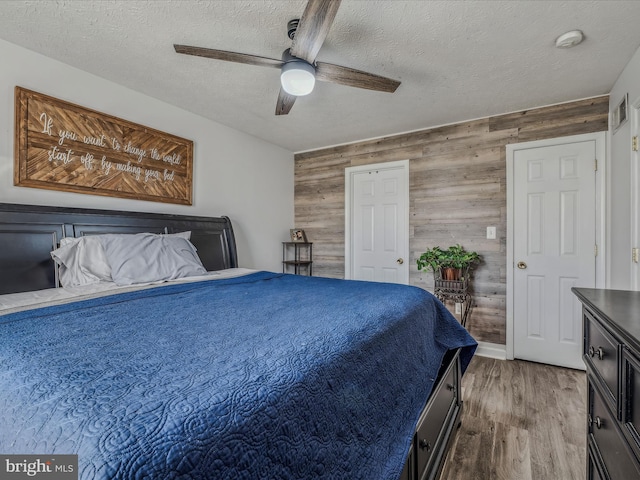 bedroom featuring a textured ceiling, hardwood / wood-style flooring, ceiling fan, and wood walls