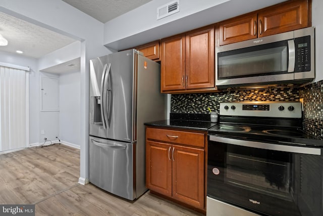 kitchen with light wood-type flooring, a textured ceiling, backsplash, and stainless steel appliances