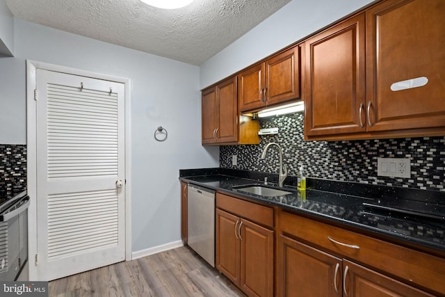 kitchen featuring dishwasher, dark stone counters, sink, a textured ceiling, and light hardwood / wood-style floors