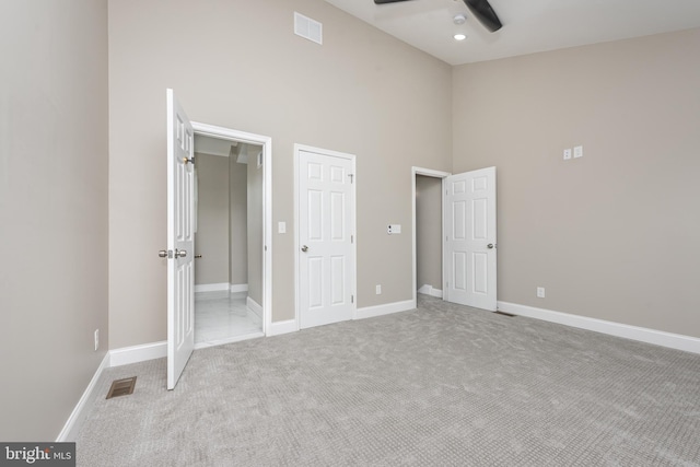 unfurnished bedroom featuring ceiling fan, a towering ceiling, and light colored carpet