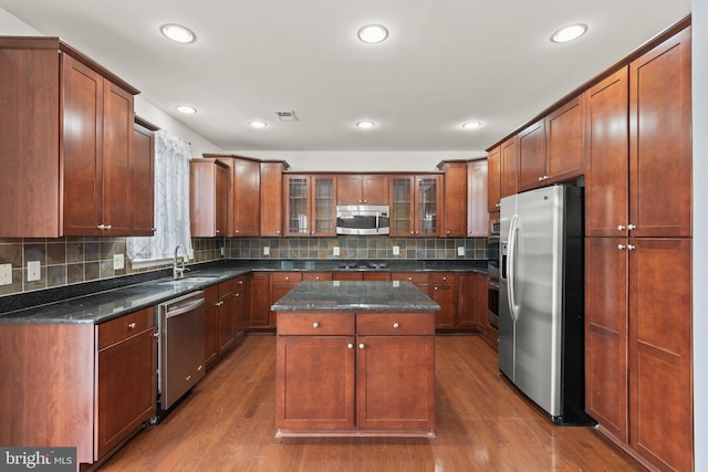 kitchen with appliances with stainless steel finishes, dark wood-type flooring, sink, dark stone countertops, and a kitchen island