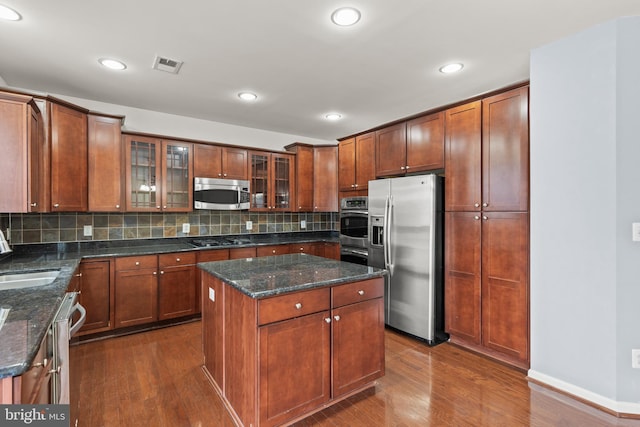 kitchen with dark hardwood / wood-style floors, a kitchen island, decorative backsplash, and stainless steel appliances