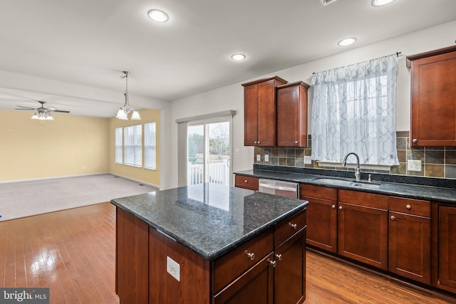 kitchen featuring ceiling fan with notable chandelier, sink, stainless steel dishwasher, decorative backsplash, and a kitchen island