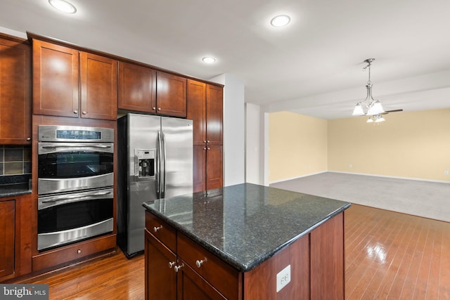 kitchen with dark stone countertops, appliances with stainless steel finishes, decorative light fixtures, a kitchen island, and a chandelier