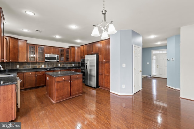 kitchen with pendant lighting, a center island, backsplash, dark wood-type flooring, and appliances with stainless steel finishes