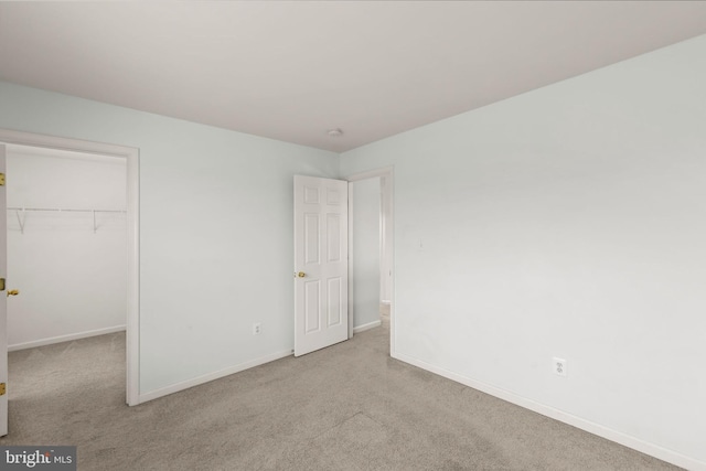 unfurnished bedroom featuring light colored carpet, a walk in closet, and a closet