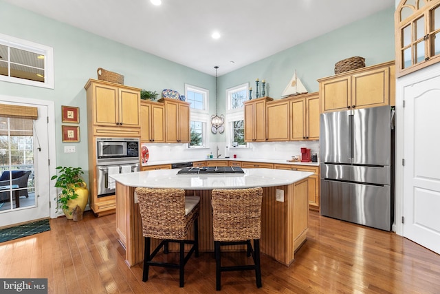 kitchen with appliances with stainless steel finishes, backsplash, pendant lighting, hardwood / wood-style flooring, and a kitchen island