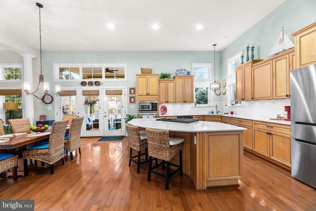 kitchen featuring backsplash, stainless steel appliances, a center island, light hardwood / wood-style floors, and hanging light fixtures