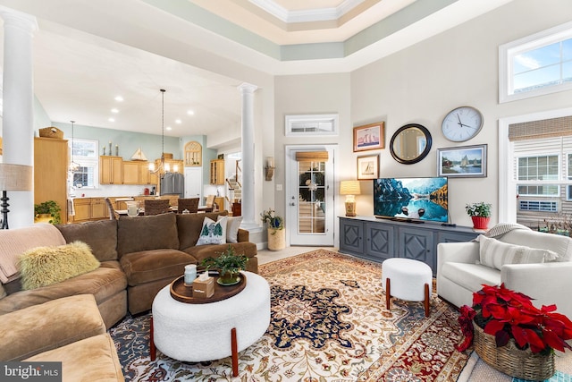 living room featuring decorative columns, ornamental molding, a high ceiling, and an inviting chandelier