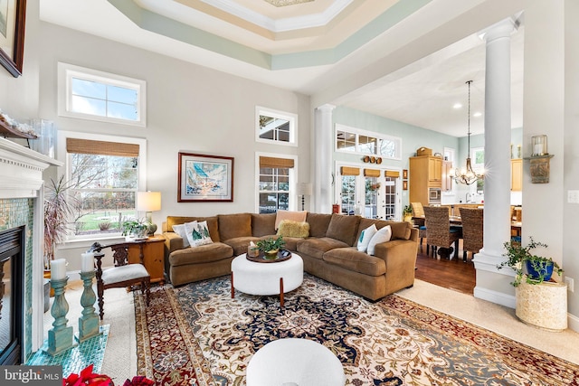 living room with a raised ceiling, a tiled fireplace, a high ceiling, and a notable chandelier