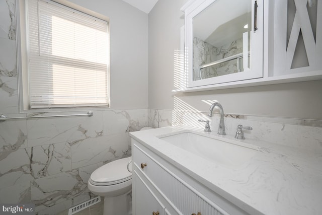 bathroom with vanity, toilet, a shower with door, and tile walls