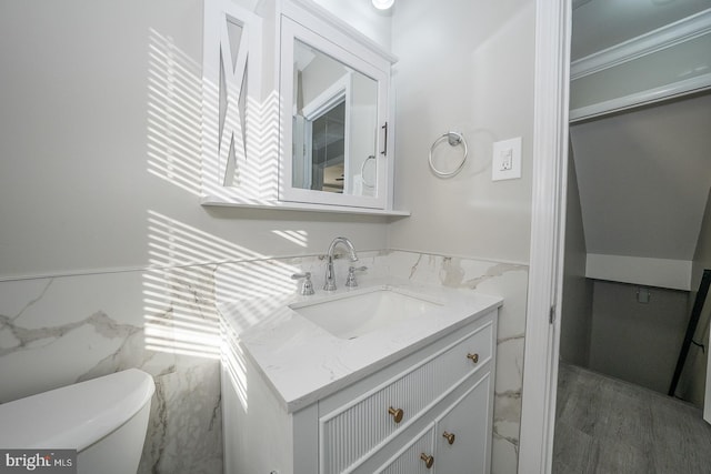 bathroom featuring wood-type flooring, toilet, vanity, tile walls, and ornamental molding