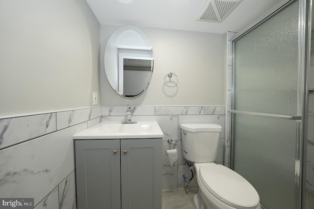 bathroom featuring vanity, toilet, a shower with door, and tile walls