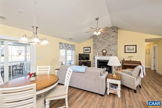 living room featuring a fireplace, light hardwood / wood-style flooring, ceiling fan with notable chandelier, and vaulted ceiling