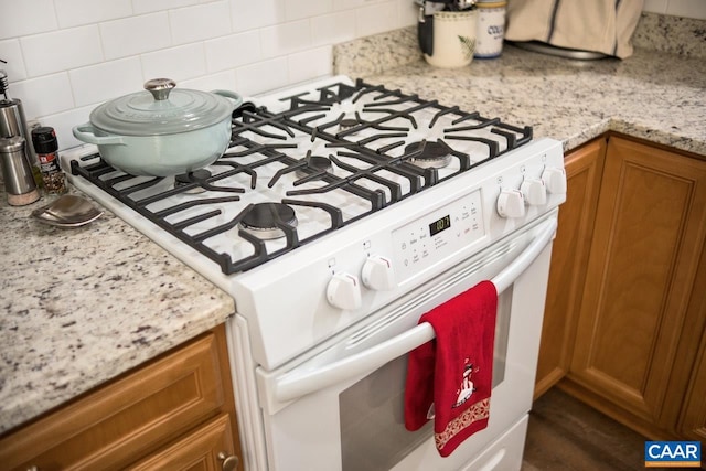 room details with decorative backsplash, light stone countertops, and gas range gas stove