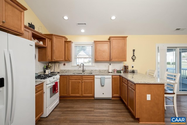 kitchen featuring white appliances, sink, dark hardwood / wood-style flooring, a kitchen bar, and kitchen peninsula