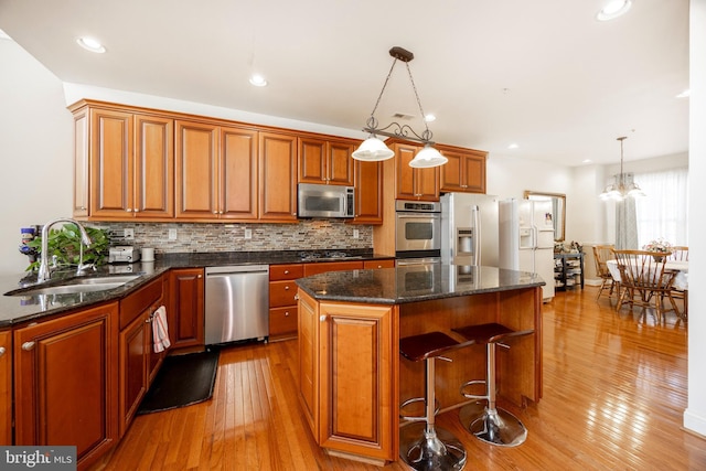 kitchen with sink, appliances with stainless steel finishes, pendant lighting, a kitchen island, and light wood-type flooring