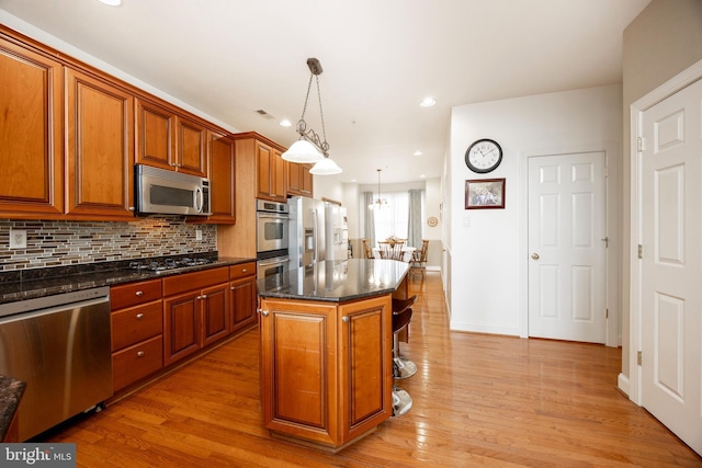 kitchen featuring backsplash, stainless steel appliances, pendant lighting, light hardwood / wood-style flooring, and a center island