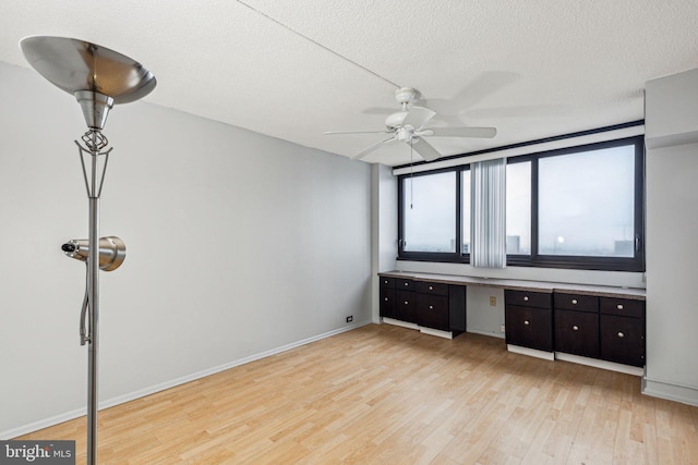 unfurnished bedroom with ceiling fan, built in desk, light hardwood / wood-style floors, and a textured ceiling