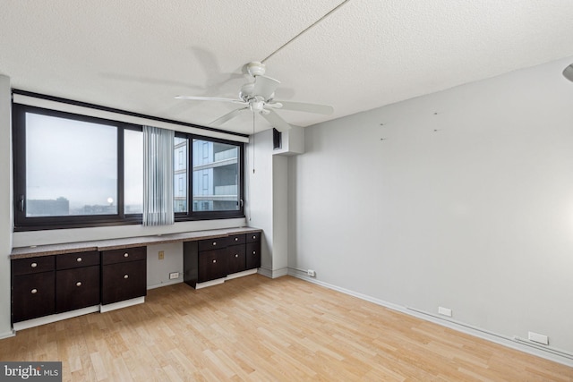 interior space with ceiling fan, light wood-type flooring, built in desk, and a textured ceiling