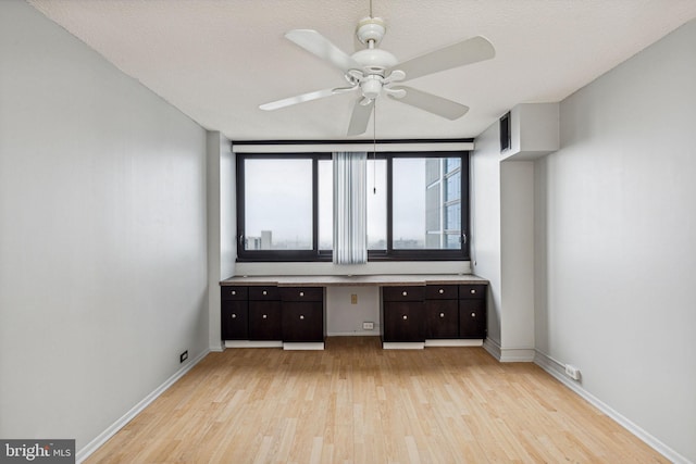 interior space featuring ceiling fan, light hardwood / wood-style floors, built in desk, and a textured ceiling