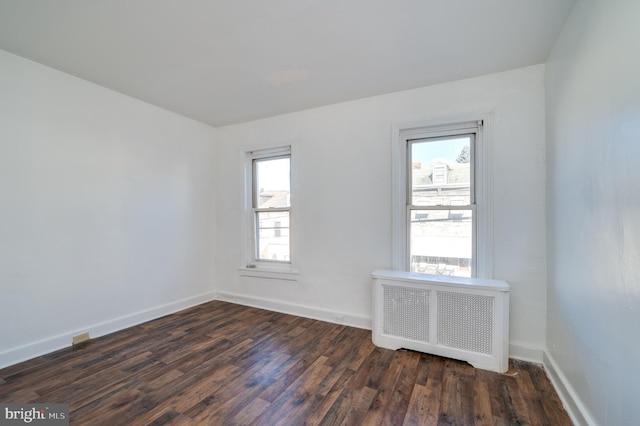 spare room with radiator heating unit, dark wood-type flooring, and a healthy amount of sunlight