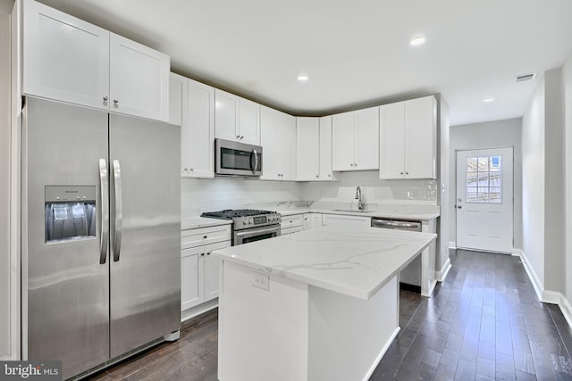 kitchen with light stone countertops, appliances with stainless steel finishes, sink, white cabinets, and a kitchen island