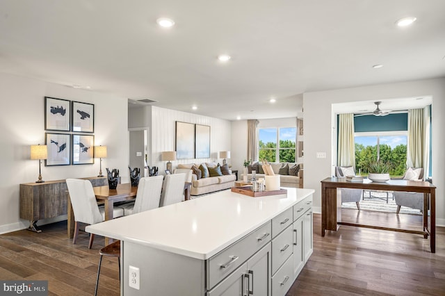 kitchen with a kitchen breakfast bar, a kitchen island, ceiling fan, and dark wood-type flooring