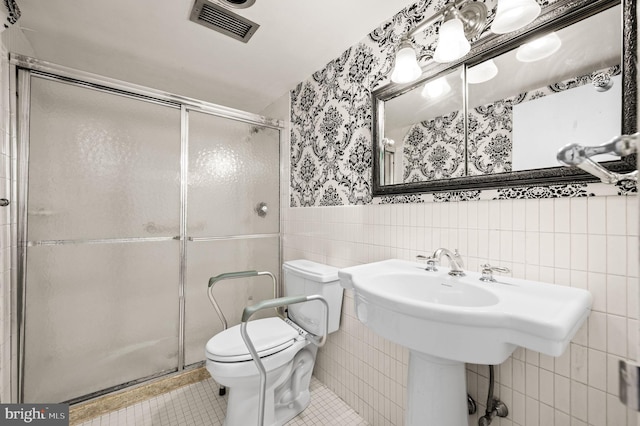 bathroom with tile walls, tile patterned floors, a shower with shower door, and toilet