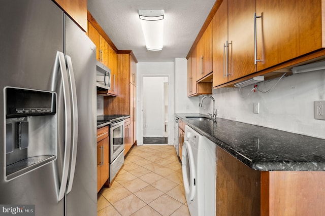 kitchen with sink, light tile patterned flooring, dark stone counters, washer / dryer, and appliances with stainless steel finishes