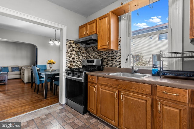 kitchen with tasteful backsplash, sink, a notable chandelier, stainless steel gas stove, and hanging light fixtures