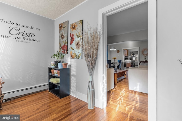 hall featuring a notable chandelier, light hardwood / wood-style flooring, a textured ceiling, and a baseboard heating unit