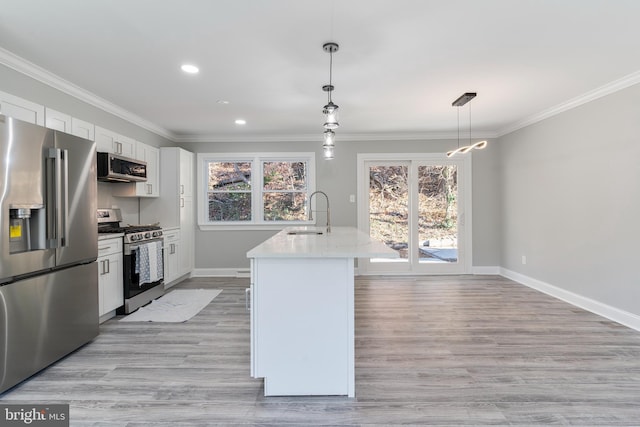 kitchen with appliances with stainless steel finishes, a kitchen island with sink, sink, pendant lighting, and white cabinets