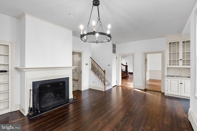 unfurnished living room featuring built in shelves, an inviting chandelier, dark wood-type flooring, and sink