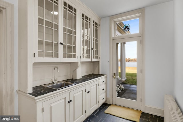 bar with radiator, white cabinets, a water view, sink, and dark tile patterned floors