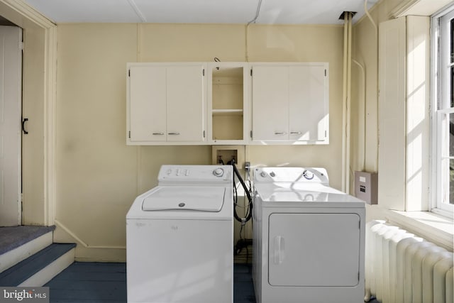 clothes washing area featuring radiator heating unit, cabinets, and independent washer and dryer