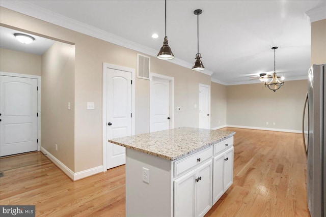 kitchen featuring a center island, stainless steel fridge, pendant lighting, light stone counters, and white cabinetry