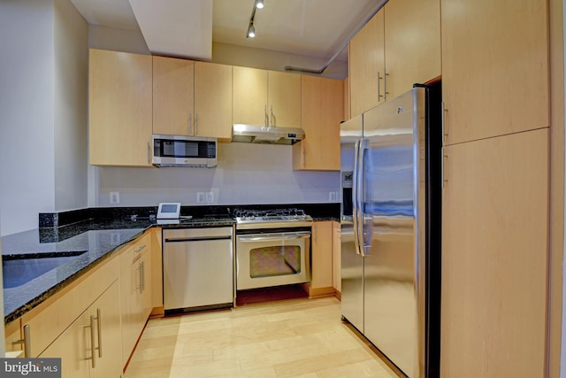 kitchen featuring light hardwood / wood-style flooring, dark stone counters, track lighting, light brown cabinetry, and appliances with stainless steel finishes