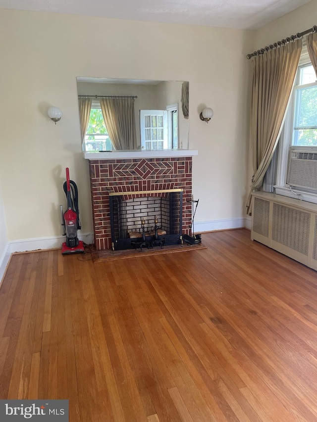 unfurnished living room featuring hardwood / wood-style flooring, radiator heating unit, a fireplace, and a wealth of natural light