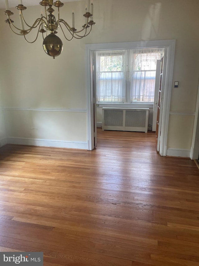 unfurnished dining area with radiator heating unit, hardwood / wood-style flooring, and a notable chandelier