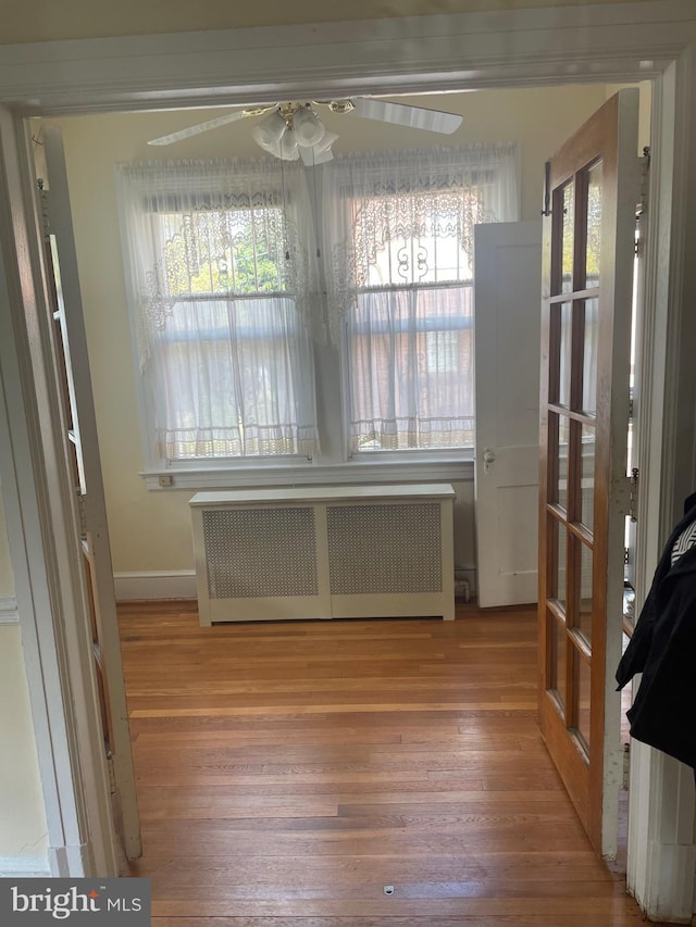 unfurnished dining area with ceiling fan, wood-type flooring, and radiator heating unit