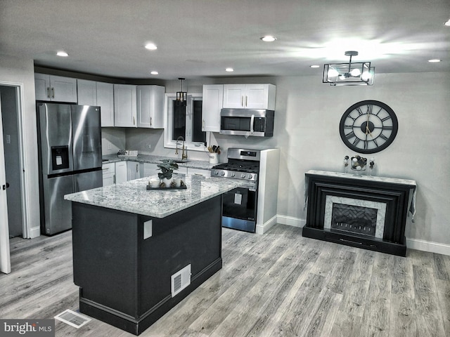 kitchen featuring white cabinets, a kitchen island, stainless steel appliances, and decorative light fixtures