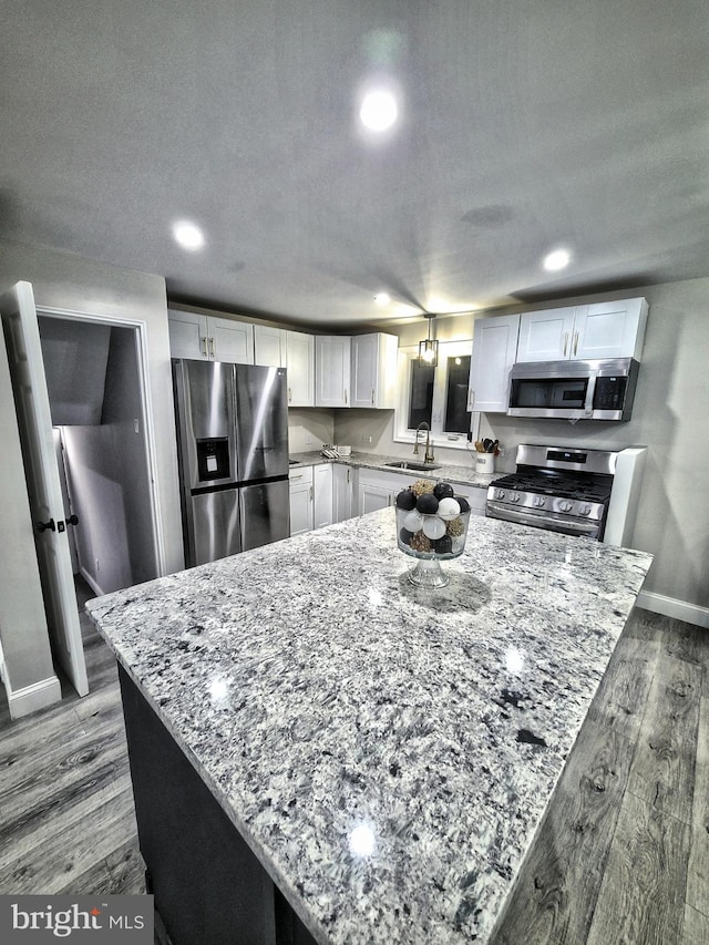 kitchen featuring white cabinets, wood-type flooring, stainless steel appliances, and light stone counters