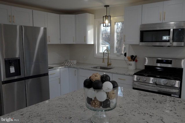 kitchen with hanging light fixtures, sink, appliances with stainless steel finishes, light stone counters, and white cabinetry