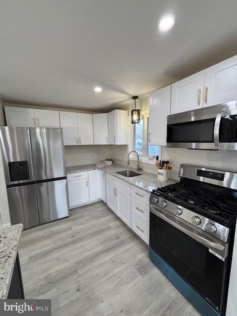 kitchen with sink, light wood-type flooring, light stone counters, white cabinetry, and stainless steel appliances