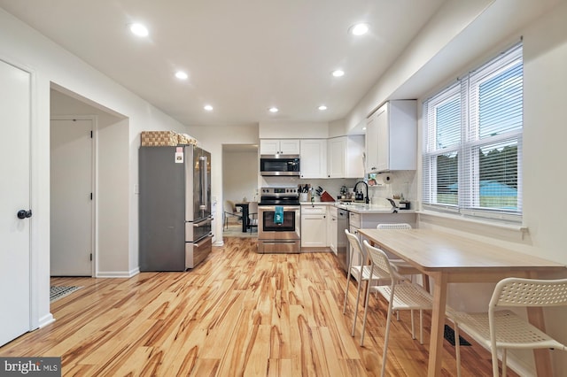 kitchen with backsplash, white cabinets, sink, light hardwood / wood-style flooring, and appliances with stainless steel finishes