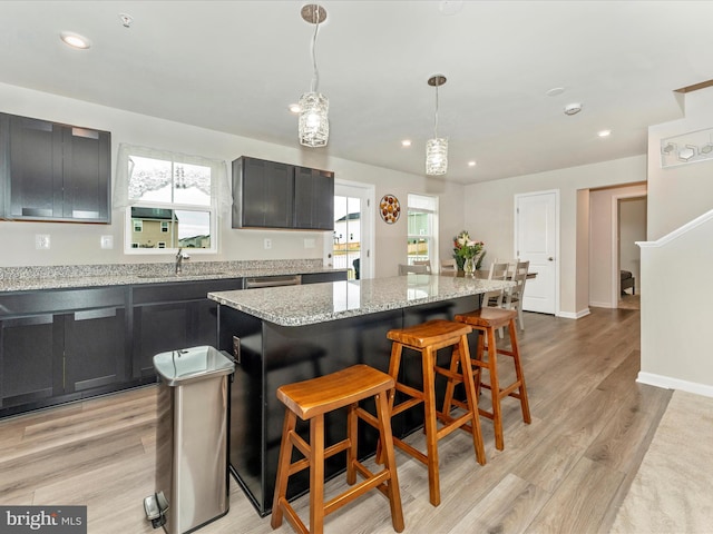 kitchen featuring light stone counters, light hardwood / wood-style flooring, a kitchen island, and hanging light fixtures