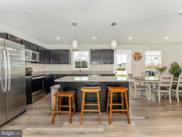 kitchen featuring light stone countertops, a kitchen island, hanging light fixtures, and appliances with stainless steel finishes